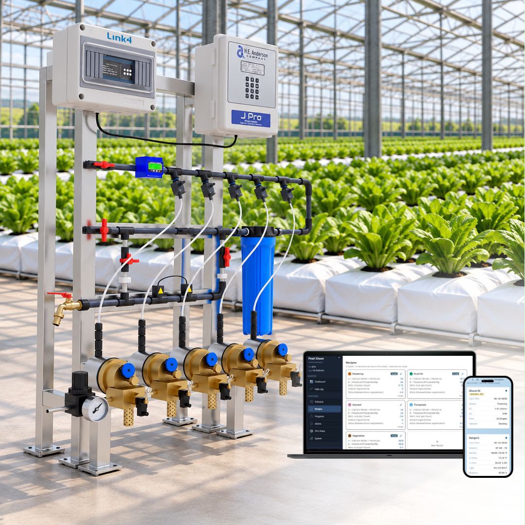 A Pearl iDoser direct injection skid standing in a commercial greenhouse, with rows of lettuce in substrate bags behind it and the iDoser console open on a laptop and a phone